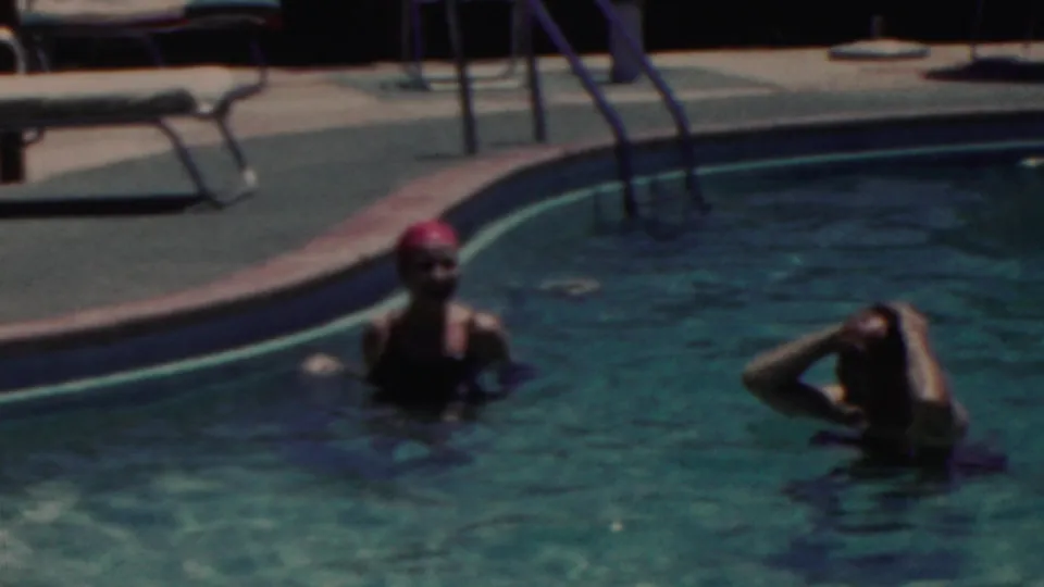 In this late frame from the 1949 Seaside, New Jersey pool footage, two women remain in the water beneath a curved edge with ladders and lounge chairs visible on the deck.