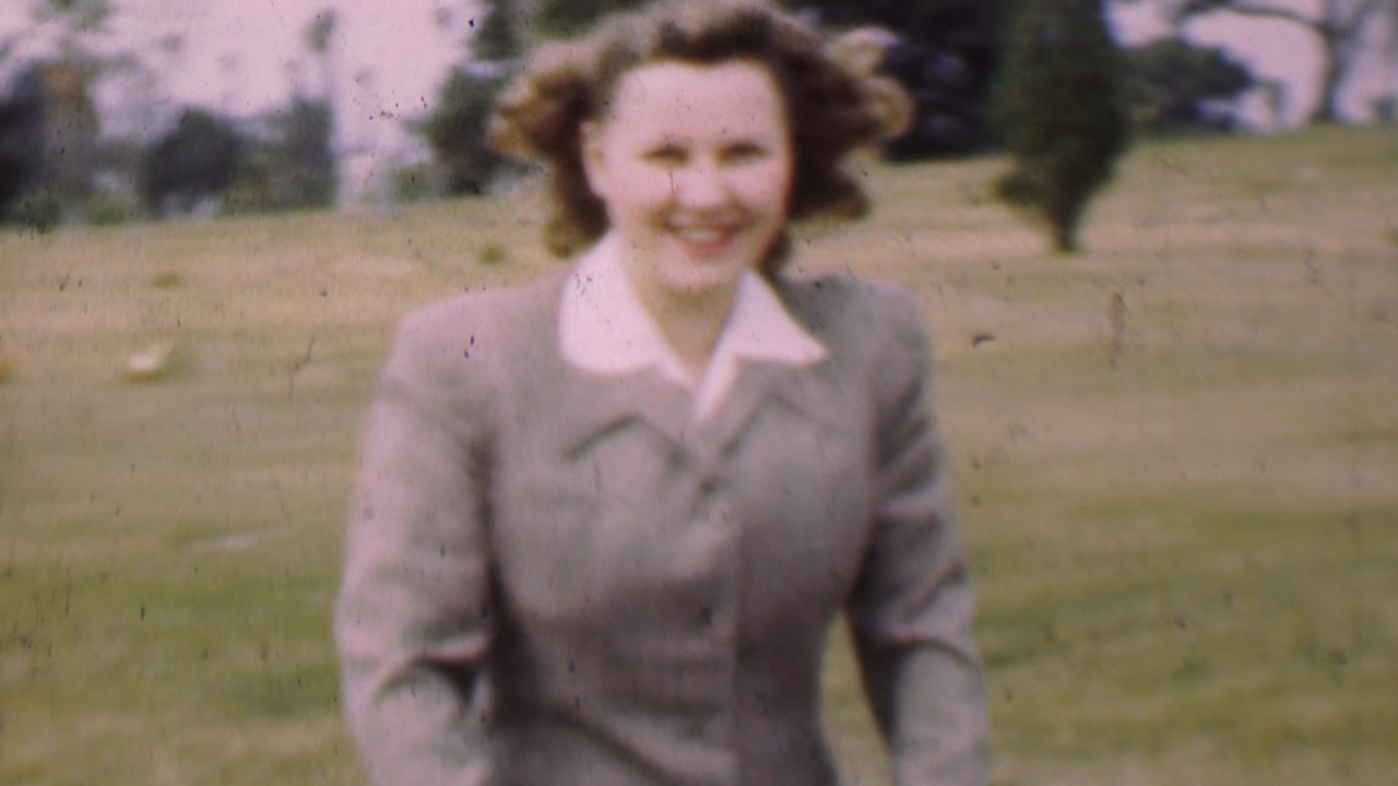 Smiling woman in a gray suit walks toward the camera in a park.
