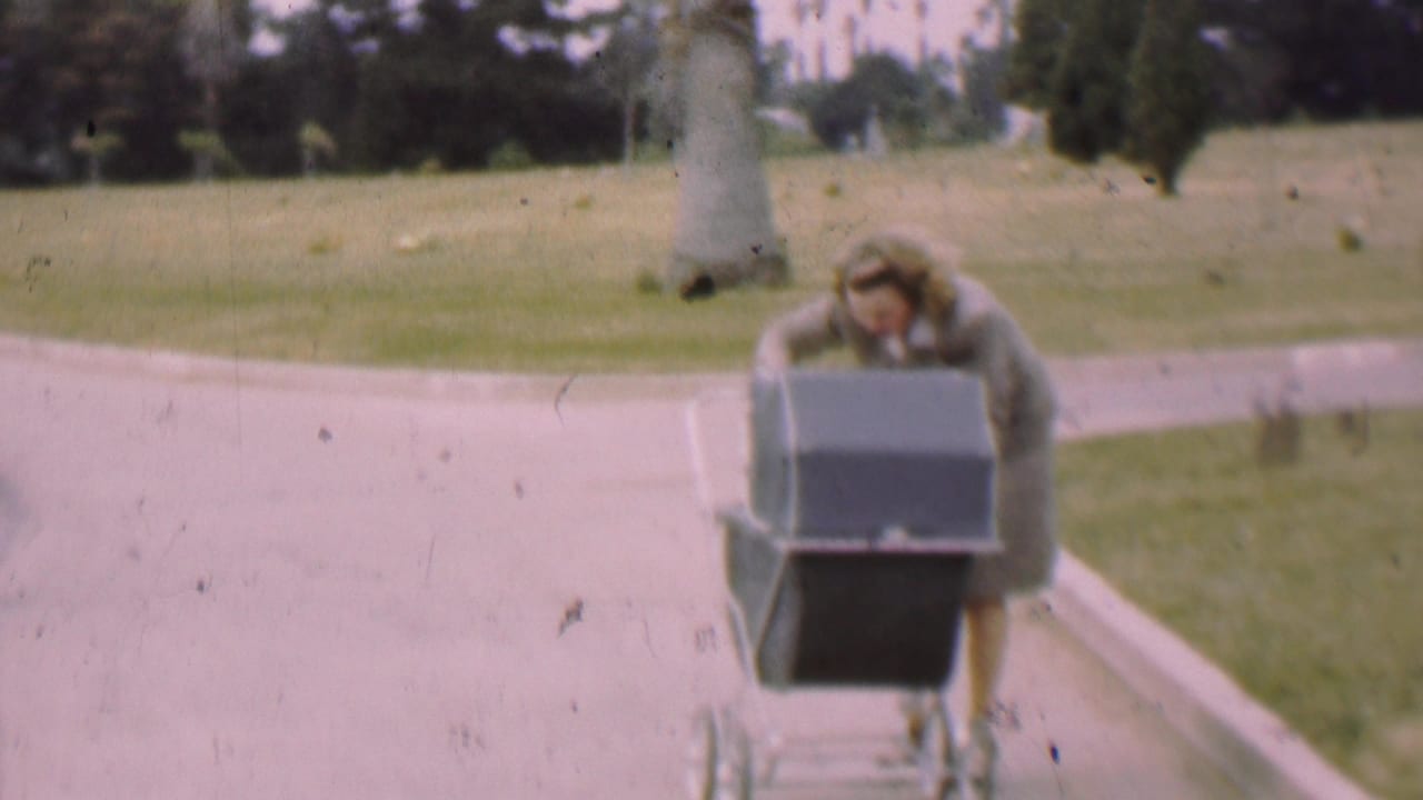 Woman leans forward behind a baby carriage on a park path.
