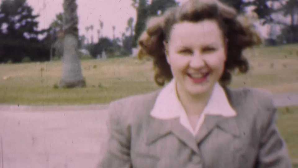 The final frame gives a close view of the smiling woman in the 1955 San Diego park footage, with her styled hair, light suit, path, lawn, and trees visible around her.