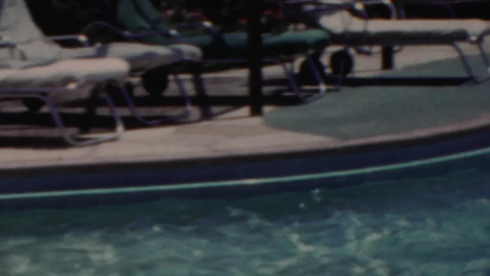The camera frames the pool edge, rippling water, and lounge chairs on the deck in the 1949 Seaside, New Jersey home-movie clip, with swimmers largely outside the visible area.