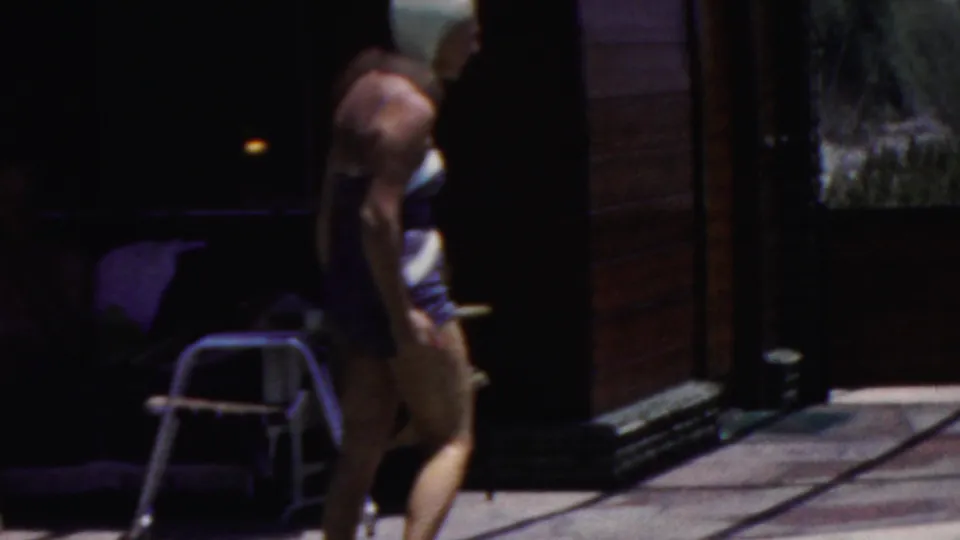 A woman in a white swim cap and dark swimsuit stands by a wooden poolside structure in the 1949 Seaside, New Jersey home-movie footage.