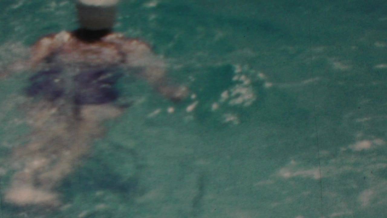 In this 1949 Seaside, New Jersey home-movie frame, a swimmer is partly submerged in rippling blue-green water with soft focus and visible film grain.