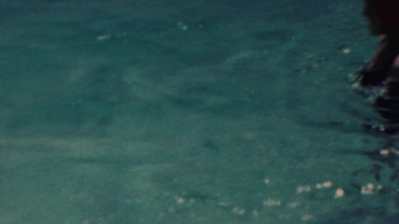 A mostly water-filled 1949 home-movie frame shows turquoise ripples and a partial swimmer or figure entering from the right edge.