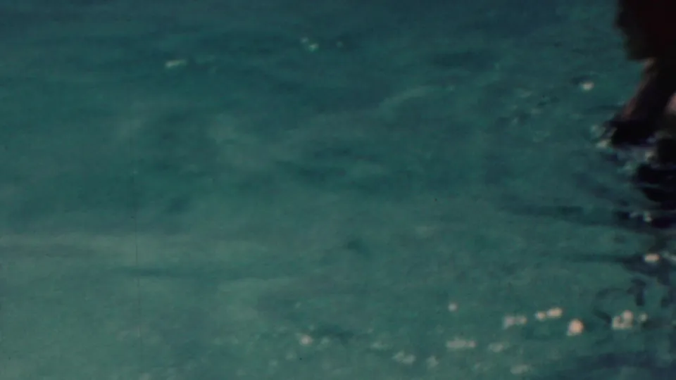 A mostly water-filled 1949 home-movie frame shows turquoise ripples and a partial swimmer or figure entering from the right edge.
