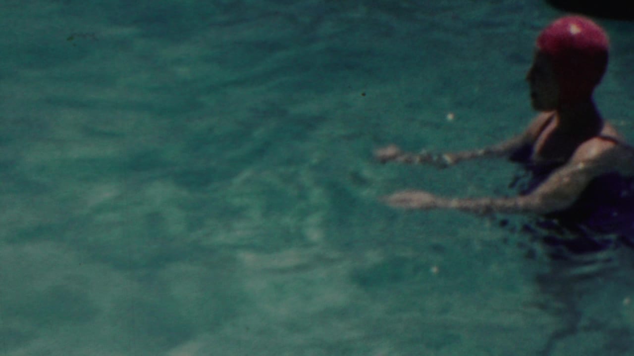 A woman wearing a red swim cap and dark swimsuit appears to wade in blue-green water in the supplied 1949 Seaside, New Jersey footage.
