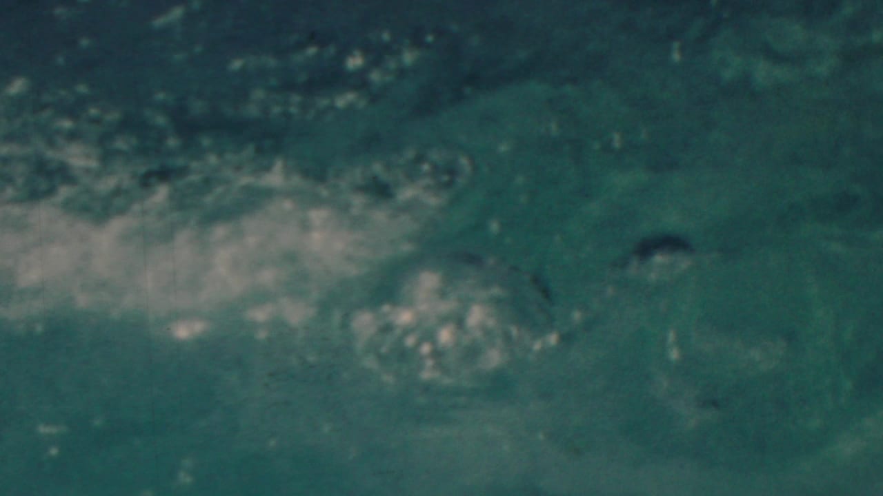 Blue-green water churns with white foam and bubbles immediately after the swimmer enters the water in this short 8mm seaside recreation sequence.