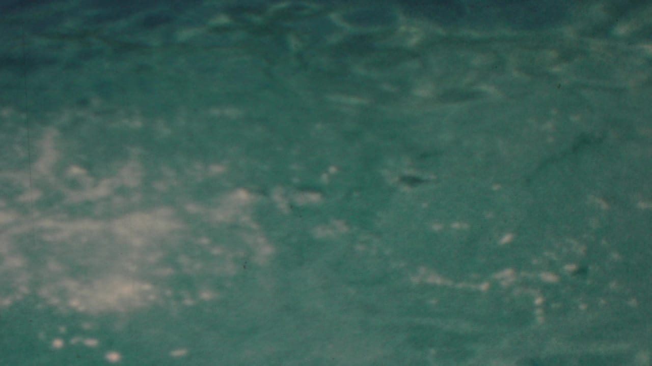 The frame is filled by turbulent blue-green water and fading white foam, closing the 1949 seaside home-movie jump sequence with an abstract splash view.