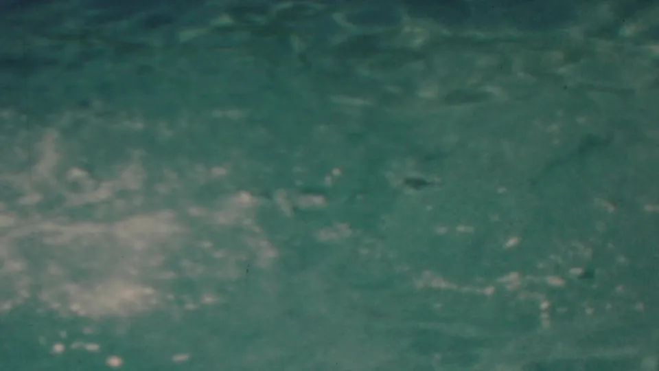 The frame is filled by turbulent blue-green water and fading white foam, closing the 1949 seaside home-movie jump sequence with an abstract splash view.