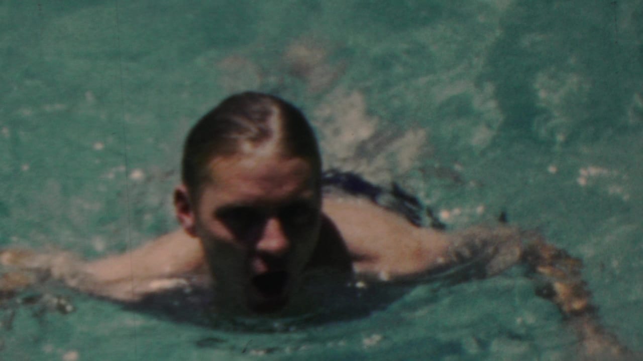 Man swimming toward the camera with arms spread in rippling pool water.