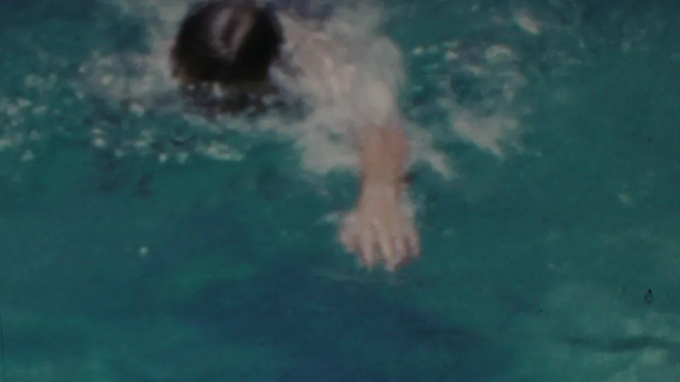 A swimmer moves through blue-green pool water in 1949 Seaside, New Jersey home-movie footage, with splashes and soft 8mm color grain obscuring some detail.