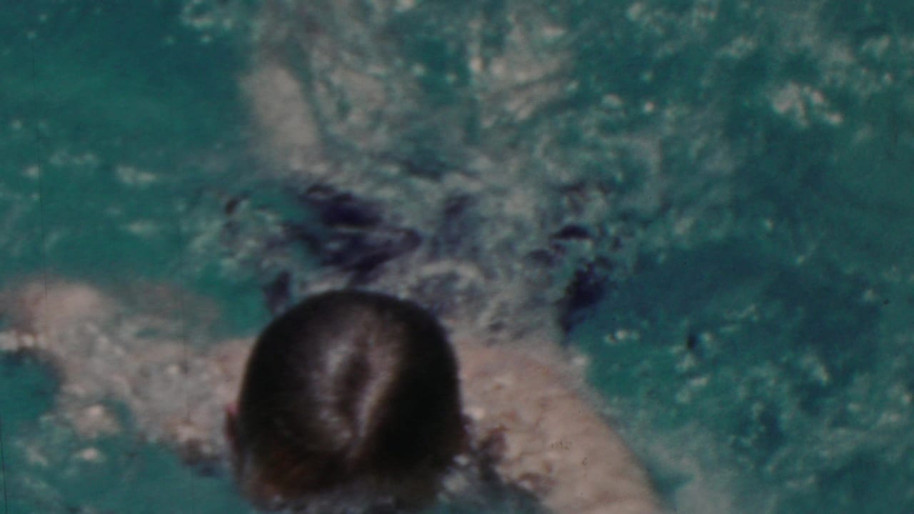 A swimmer with wet dark hair moves through turquoise pool water, seen from above in the metadata-supported 1949 Seaside, New Jersey home-movie clip.