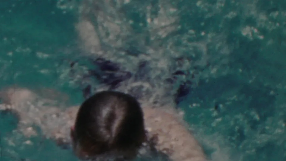 A swimmer with wet dark hair moves through turquoise pool water, seen from above in the metadata-supported 1949 Seaside, New Jersey home-movie clip.