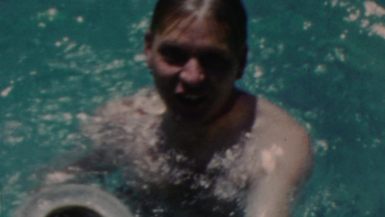 A swimmer faces the camera in blue-green pool water, with facial details softened by shadow, motion, and faded 8mm color.