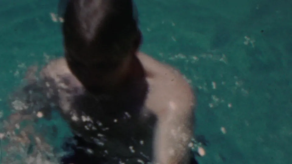 A swimmer with slicked dark hair and bare shoulders is partly submerged in sunlit pool water in the short Seaside, New Jersey home-movie sequence.