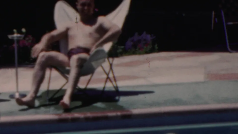 In Seaside, New Jersey, 1949, a shirtless man in dark swim trunks sits in a white folding chair near the edge of a backyard swimming pool.
