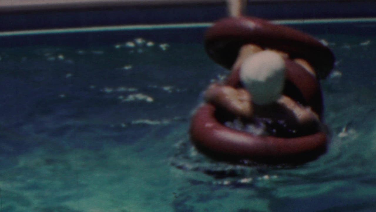 A swimmer, likely a child based on scale and metadata, wears a white swim cap and holds a red inflatable ring in the blue-green pool water in Seaside, New Jersey, 1949.