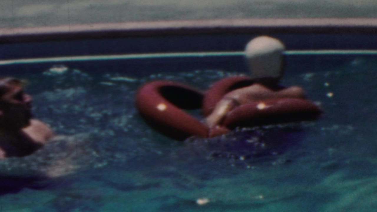 1949 Seaside, New Jersey home-movie frame showing swimmers in a blue pool, including one person wearing a light swim cap while floating on a red inflatable ring.