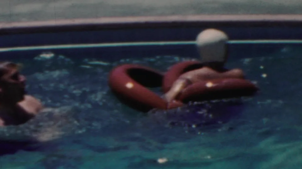 1949 Seaside, New Jersey home-movie frame showing swimmers in a blue pool, including one person wearing a light swim cap while floating on a red inflatable ring.