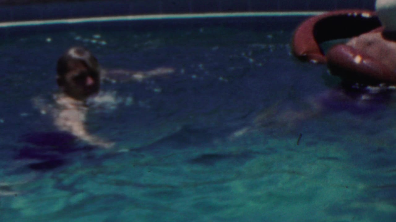 A swimmer faces the camera in a pool near red inflatable rings.