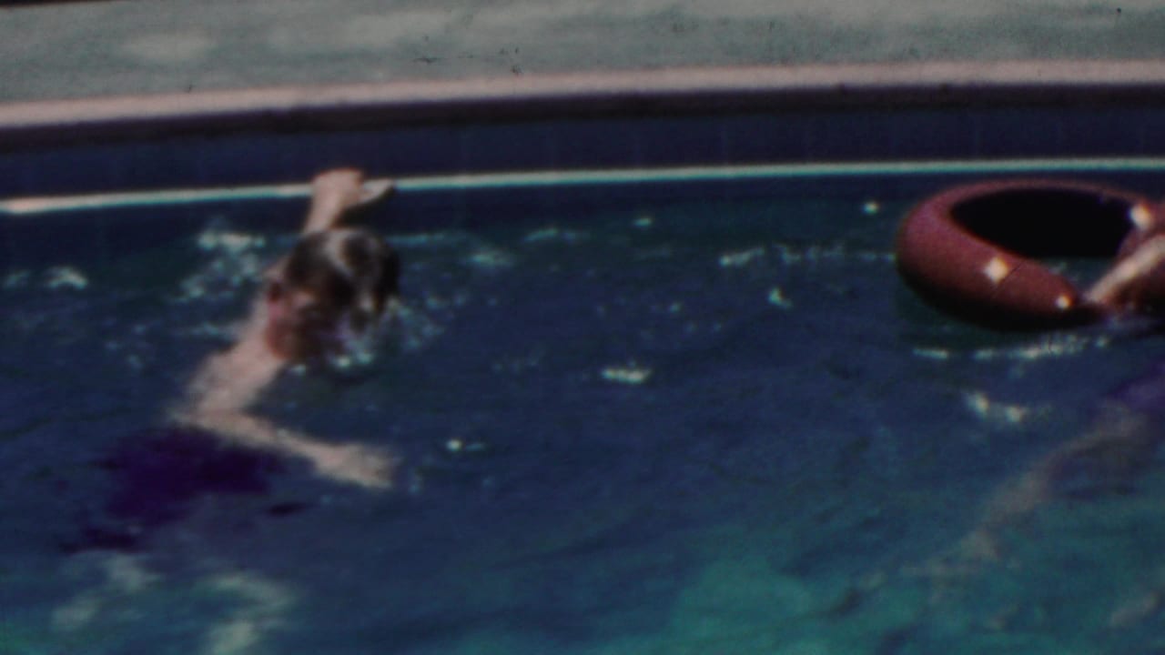 1949 Seaside, New Jersey home-movie frame showing a swimmer moving through blue water toward a red inflatable ring near the concrete pool edge.