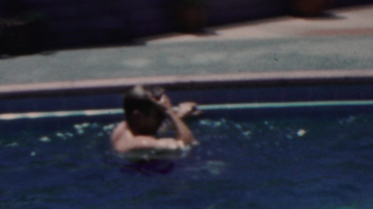 1949 Seaside, New Jersey home-movie frame showing a swimmer near the concrete pool edge with one arm raised to their head in sunlit blue water.