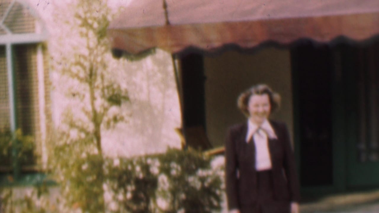 Woman smiling in front of a shaded doorway and awning with greenery nearby.