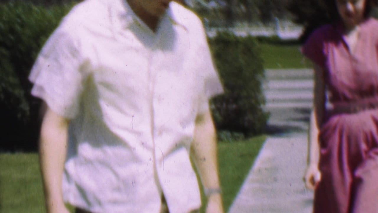 Close crop of a man in a white shirt walking beside a woman in a pink dress.