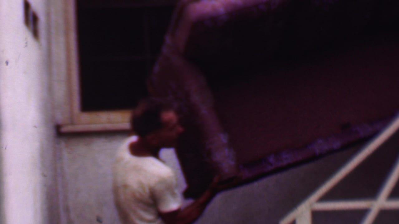 Man partly hidden by a large couch while carrying it down exterior stairs.