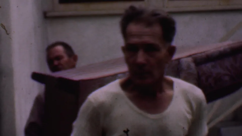 At the end of the 1956 Phoenix clip, one man faces the camera while another remains partly hidden behind the purple couch near the exterior staircase.