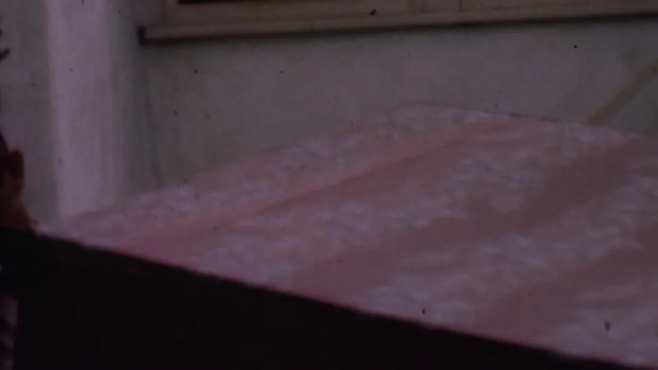 A man in a light shirt is partly hidden behind a bulky wooden desk or cabinet as it is carried along a stucco building exterior in the 1956 Phoenix clip.