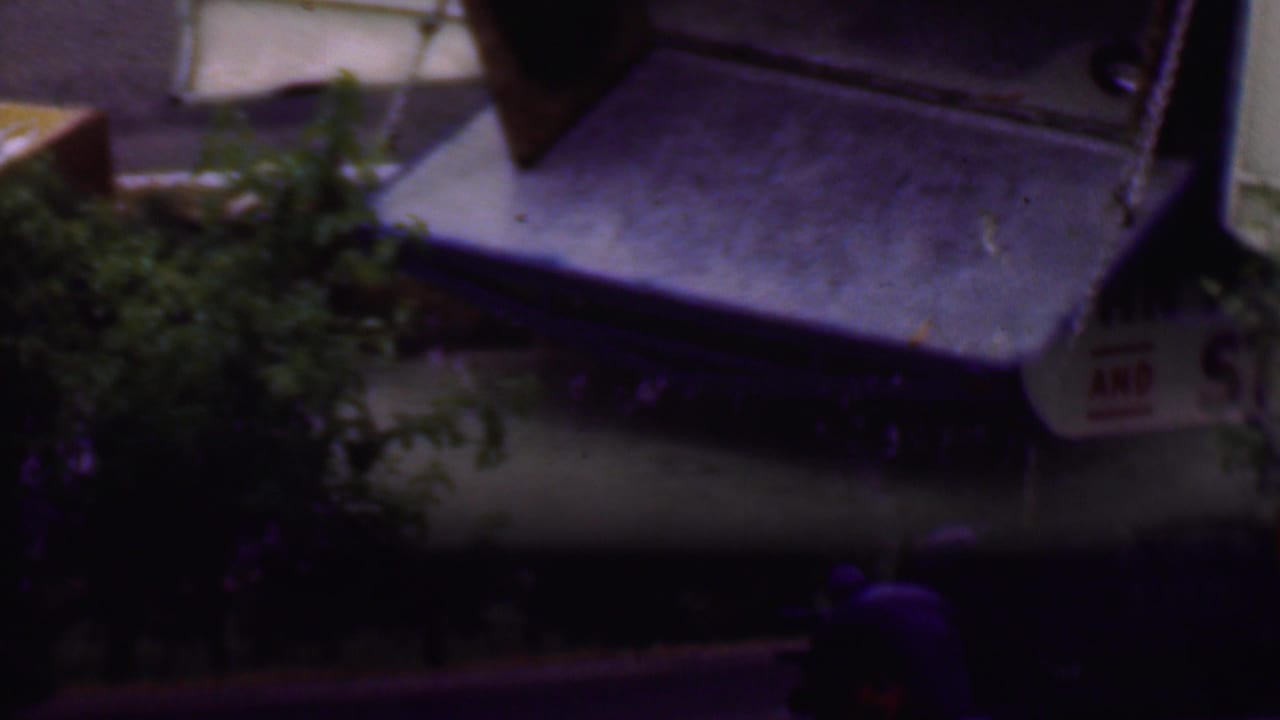 1956 Phoenix 8mm frame showing a blue Pan American Van and Storage Co moving truck partly cut off as it passes along a tree-lined road.