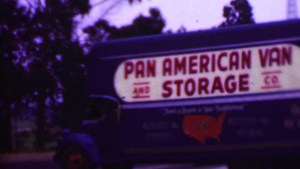 1956 Phoenix 8mm frame showing the broad side of a blue Pan American Van and Storage Co moving truck, including red sign lettering and a red United States map graphic.