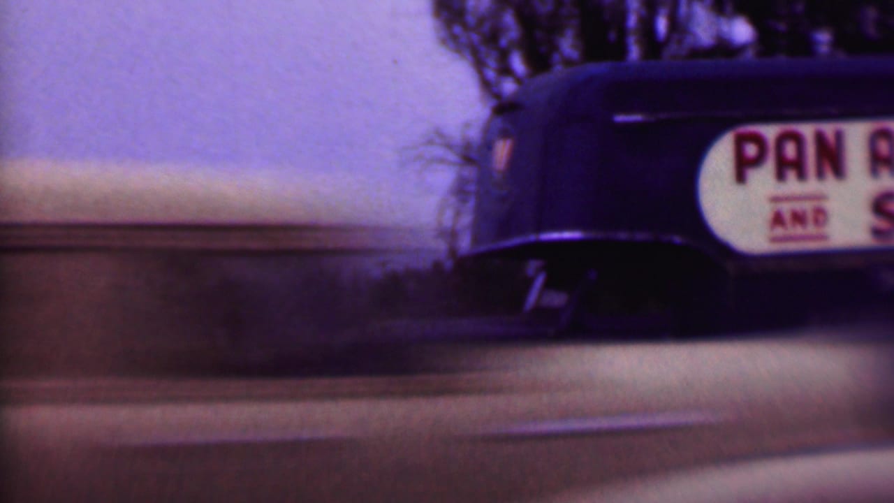 1956 Phoenix home-movie frame showing a dark Pan American Van and Storage truck partly cropped as it moves past a residential street with trees in the background.