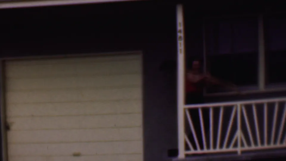 A partly obscured view shows the woman near the porch and garage of the Phoenix suburban house, framed by white railings and vertical posts.