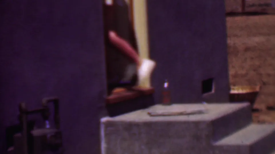 Phoenix 1956 8mm frame showing a cropped person in white shoes on a concrete step beside a doorway and exterior wall.