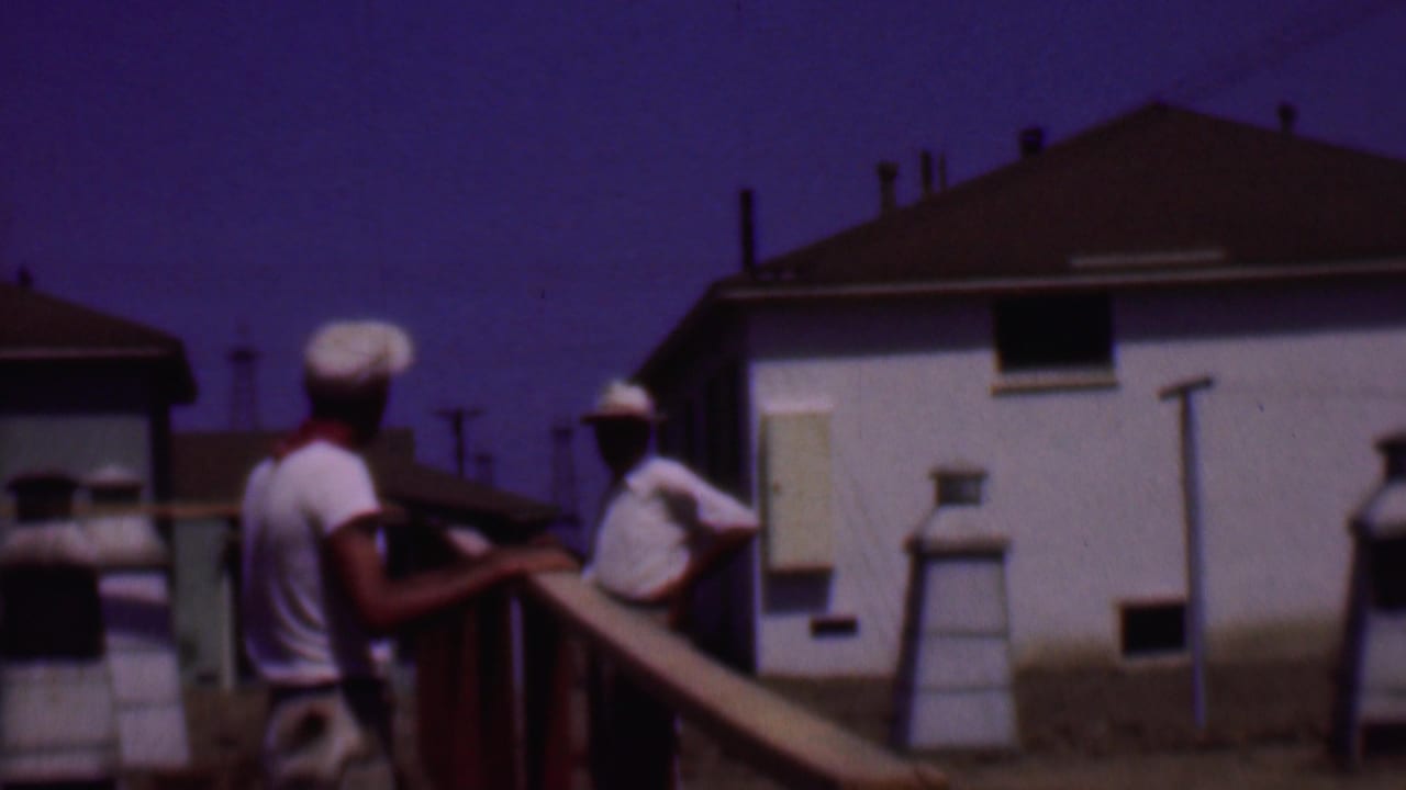 A 1956 Phoenix residential scene shows two men handling long boards near a wooden frame, with low houses and utility poles in the background.