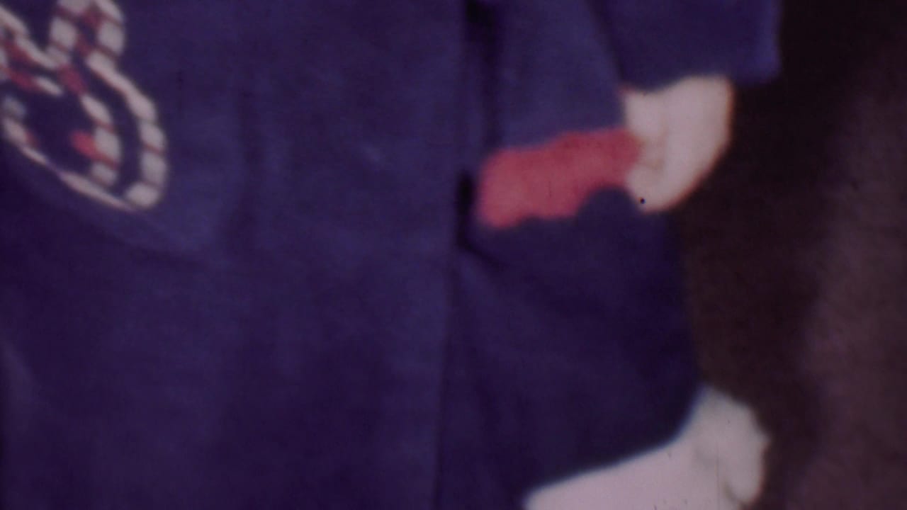 Close 1956 Phoenix home-movie frame showing part of a young child in a dark blue bathrobe, with a small red and white patch partly visible at the left edge.