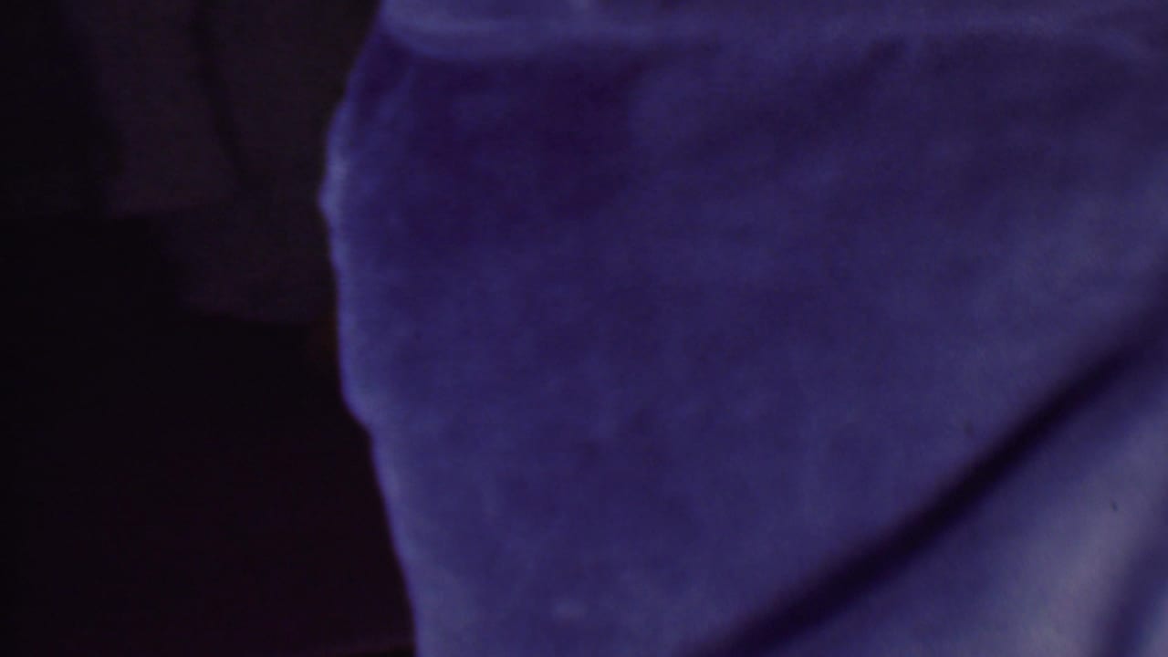 A tightly cropped 1956 Phoenix 8mm frame shows blue-purple textured fabric covering a woman's shoulder or head area, with her face mostly outside the frame.