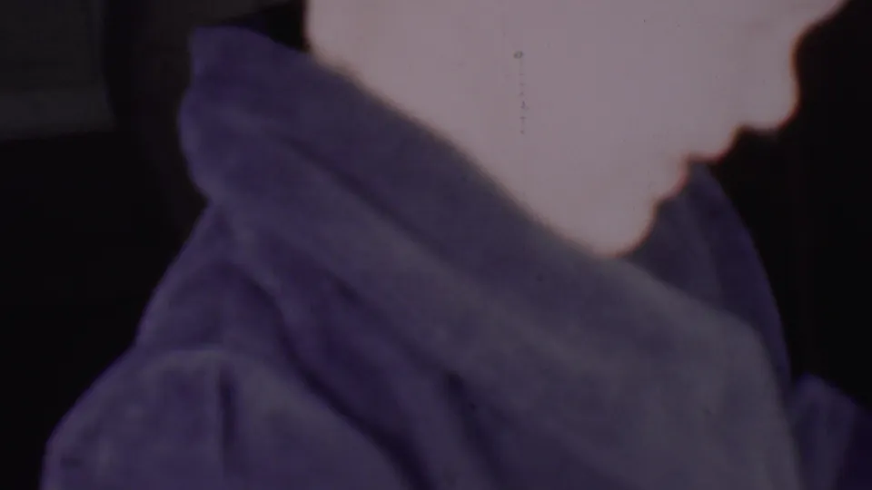 The 1956 Phoenix 8mm frame shows an adult woman in soft profile with a blue-purple covering around her head and shoulders, photographed very close and slightly blurred.