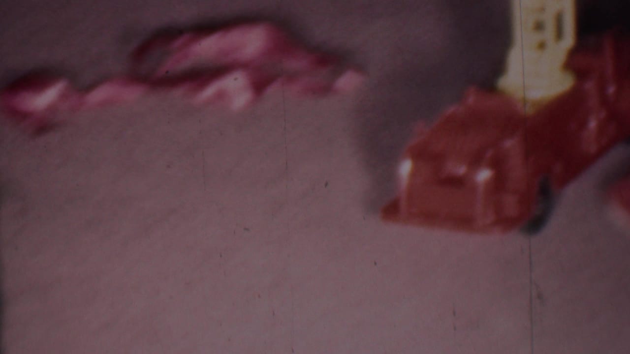 Soft 8mm frame from the 1956 Phoenix Christmas home-movie clip showing a cropped red toy fire engine with a yellow ladder on a carpeted floor.
