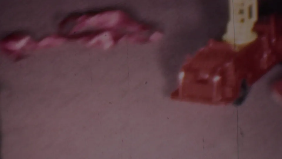 Soft 8mm frame from the 1956 Phoenix Christmas home-movie clip showing a cropped red toy fire engine with a yellow ladder on a carpeted floor.