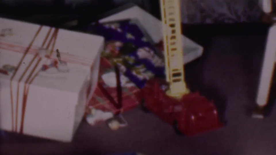 The red toy fire engine stands beside wrapped Christmas presents, including a white box with red ribbon, in the 1956 Phoenix home-movie clip.