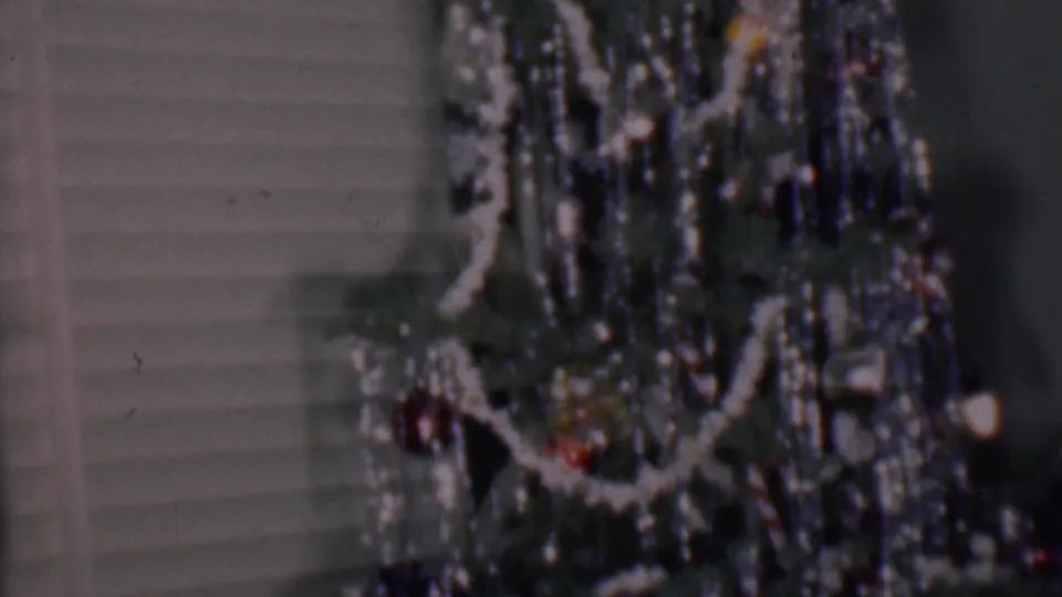 Phoenix, Arizona 1956 frame of a close indoor Christmas tree view with curved white garland, shiny tinsel, small colored ornaments, and white horizontal blinds.