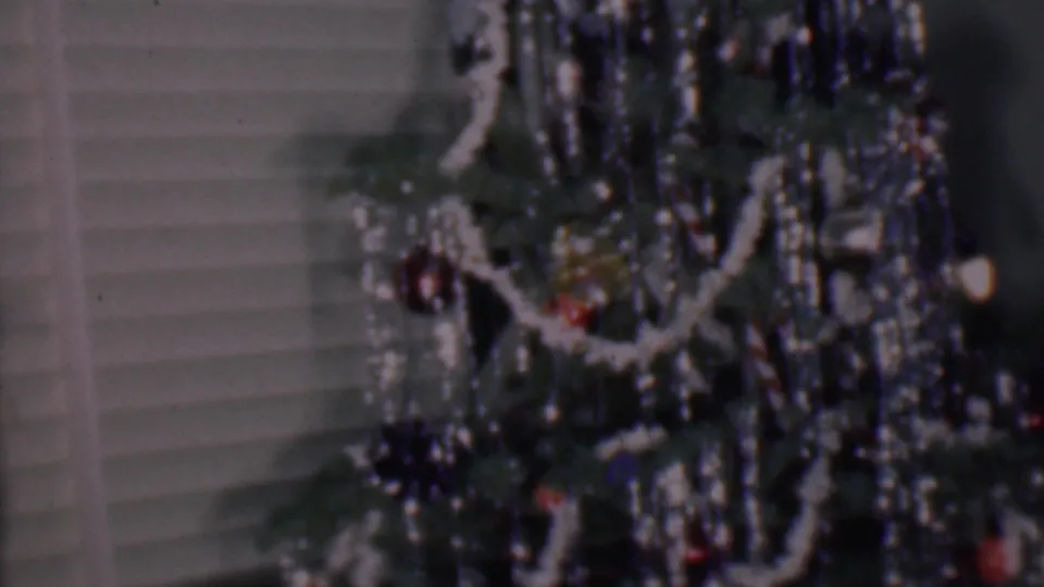 Phoenix, Arizona 1956 home-movie frame showing a lower portion of the indoor Christmas tree with white garland, dense tinsel, red ornaments, and soft film blur.