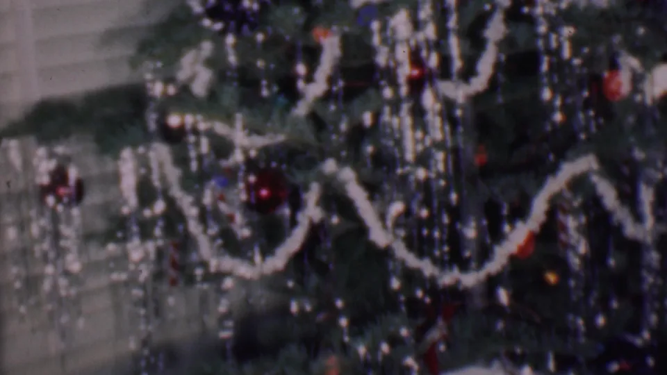Close 1956 Phoenix home-movie frame of Christmas tree decorations, including white garland loops, red and dark ornaments, and dense reflective tinsel-like strands.