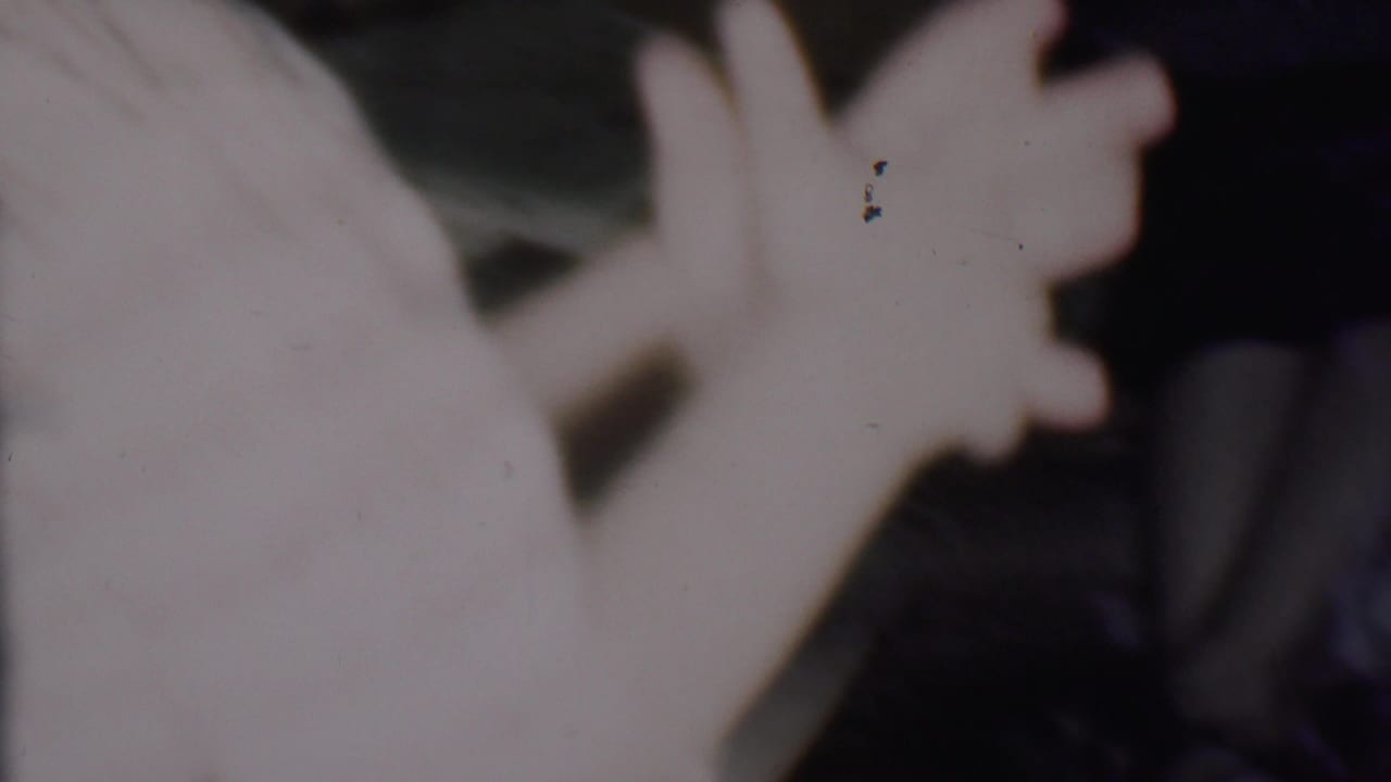 Faded 8mm frame from the supplied 1956 Phoenix home-movie clip showing a soft, overexposed close-up with a pale hand or arm near dark green foliage or decoration.