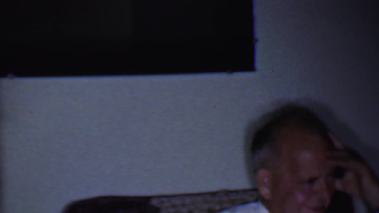 Seated adult man laughing near a wall, with his hand beside his head.