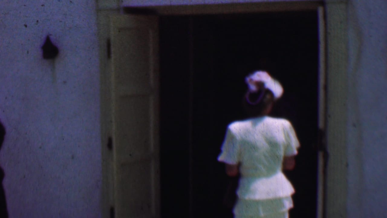 In 1956 Dallas home-movie footage, a woman in a white dress and hat approaches or pauses at the open doorway of a white church building.