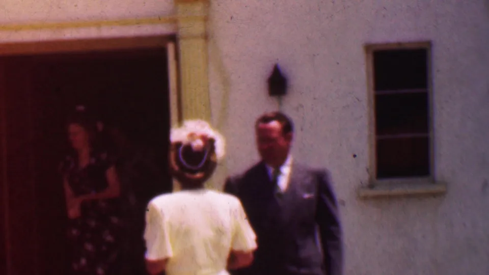 A woman in a white dress and hat faces a man in a suit outside the Dallas church entrance, with another woman in a floral dress visible in the doorway.